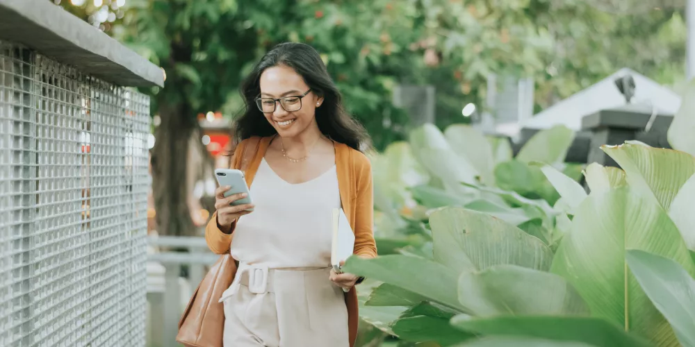 Jeune femme souriante marchant dans la rue un téléphone à la main