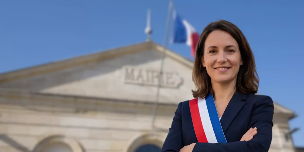 Élue municipale devant une mairie illustrant la communication municipale avec les citoyens d’une commune