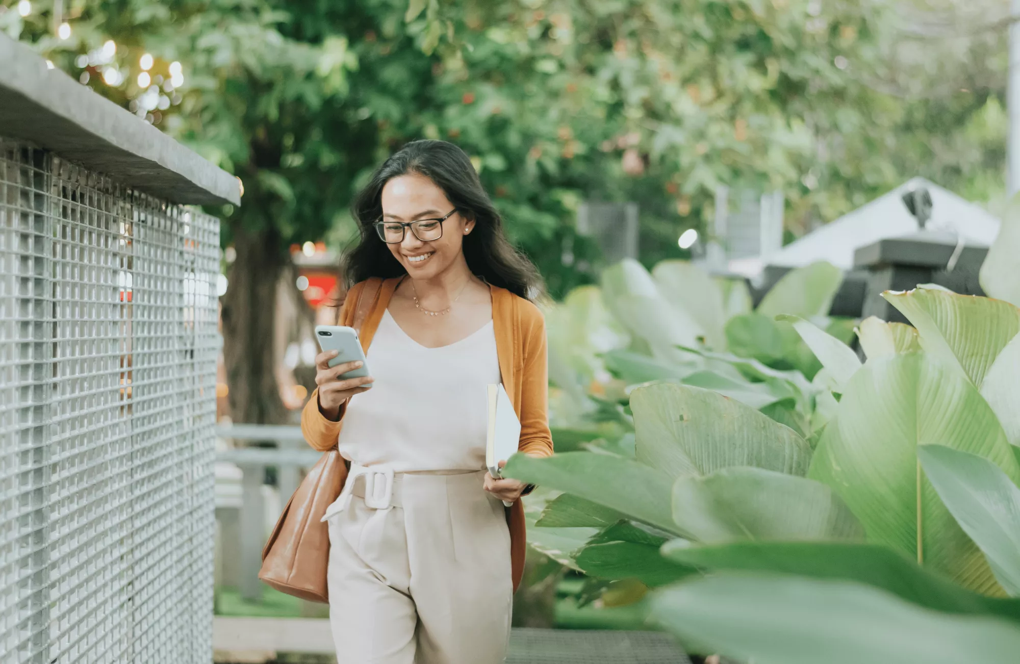 Jeune femme souriante marchant dans la rue un téléphone à la main